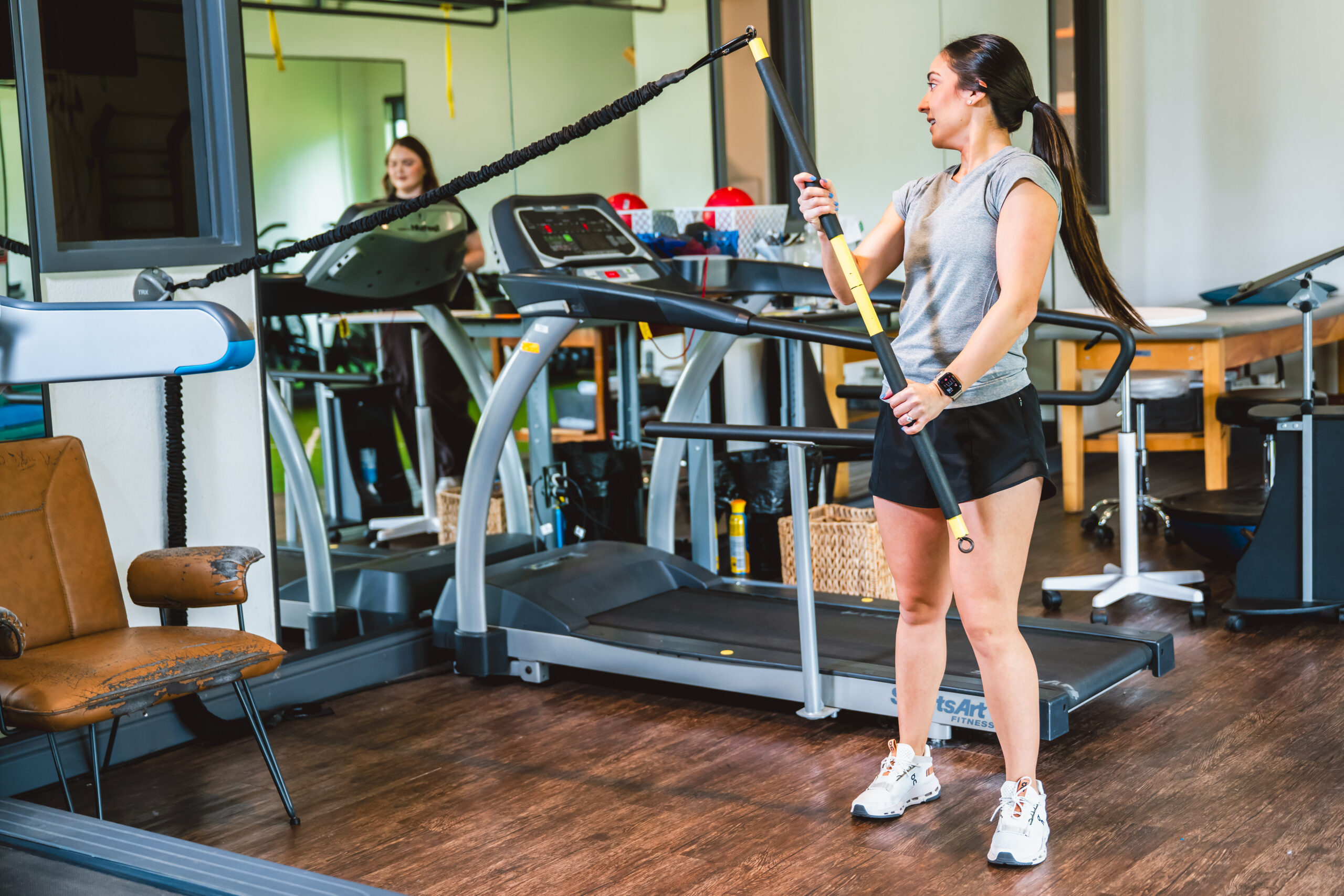 Female athlete using resistance bands in a modern fitness studio, focusing on performance and rehabilitation, with gym equipment visible in the background, emphasizing sports physical therapy and personalized care.